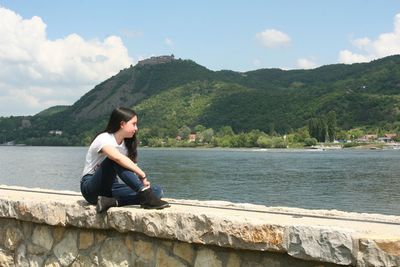 Side view of woman sitting on mountain against sky