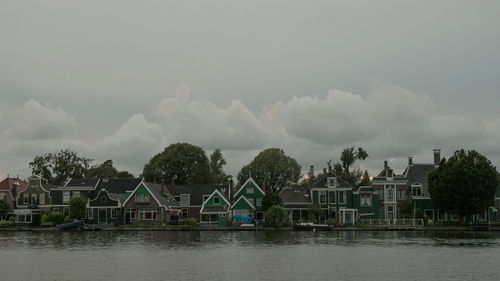 Houses and trees by lake against sky