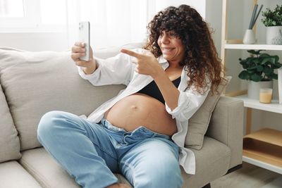 Young woman using mobile phone while sitting on sofa at home