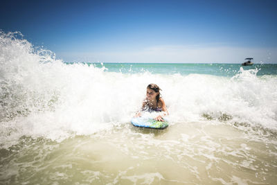 Girl surfing in sea against clear sky