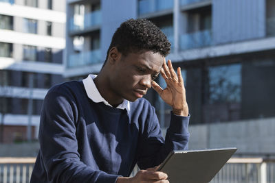 Serious young man with digital tablet against building