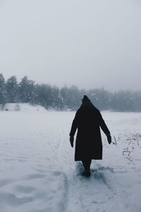 Rear view of person walking on snow against sky