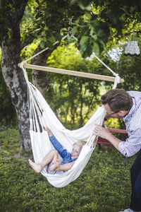 Playful father swinging cheerful son in yard