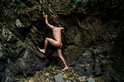 Naked man climbing rock formation