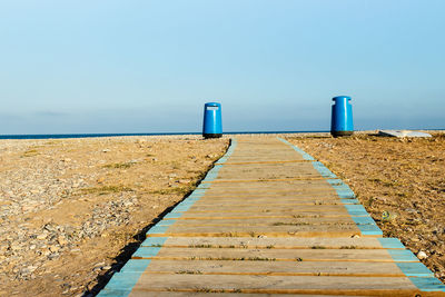 Surface level of wooden walkway by sea against sky