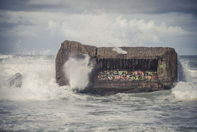 Sea waves splashing on rock formation against sky