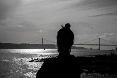Rear view of man looking at suspension bridge over sea