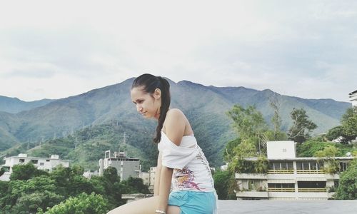 Side view of young woman standing on retaining wall against mountains