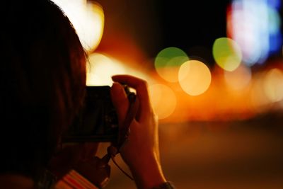 Close-up of woman photographing on city street at night