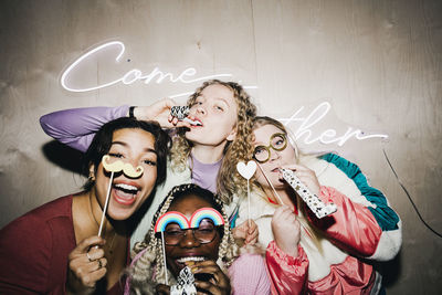 Portrait of carefree multiracial female friends with props enjoying in college dorm