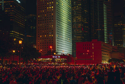 People on illuminated road amidst buildings at night