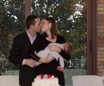 Couple kissing while holding baby at home