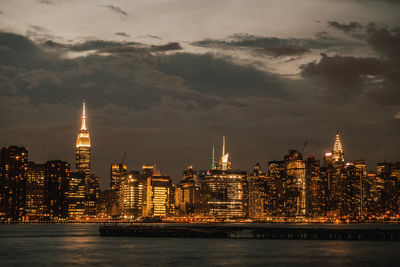 Illuminated buildings by river against sky at night