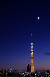 Illuminated tower in city against clear blue sky at night