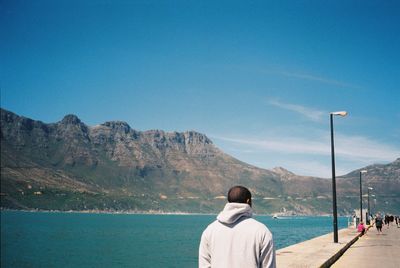 Rear view of man looking at sea against mountain range