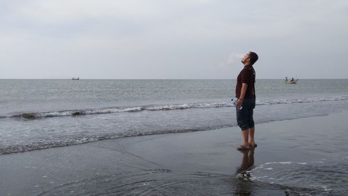 Man igniting smoke while standing on shore at beach against sky