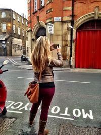 Rear view of woman photographing on street in city