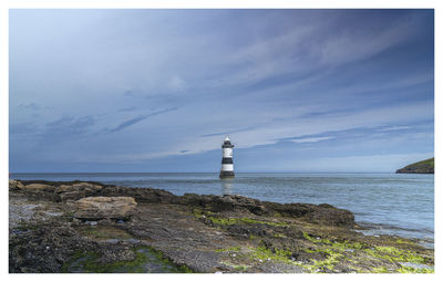 Lighthouse by sea against sky