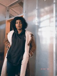 Portrait of young woman looking away while standing against wall