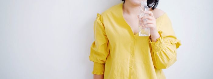 Midsection of woman standing against yellow wall