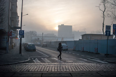 Full length of woman crossing city street against sky during foggy weather