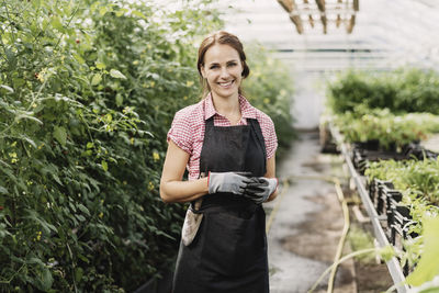 Portrait of smiling female gardener standing in greenhouse