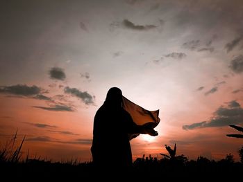 Silhouette woman standing against orange sky during sunset