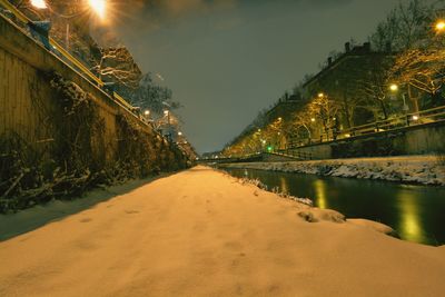 Illuminated road amidst trees against sky at night