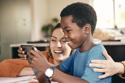 Happy mother with arm around son enjoying while watching digital tablet at home