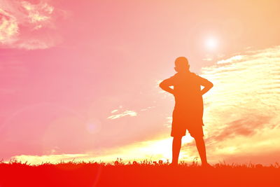 Silhouette boy standing with hands on hips against sky during sunset