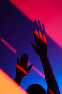 Woman arm gesturing with open hand over fashion blue, orange and pink wall, neon red light on wrist