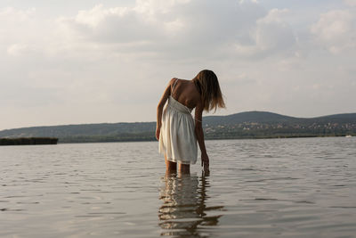 Rear view of woman standing in sea against cloudy sky