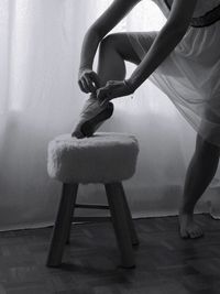 Low section of woman wearing ballet shoe on stool at home