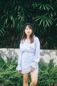 Portrait of beautiful young woman standing against plants