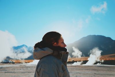 Profile view of woman wearing jacket while standing against blue sky