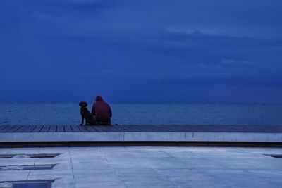 Rear view of people sitting by swimming pool against sky