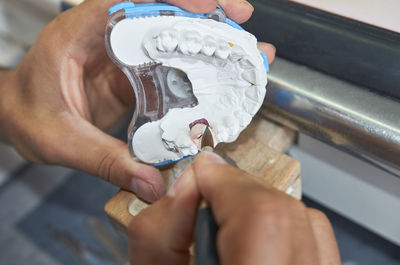 Cropped image of dentist using paintbrush while holding dental mold