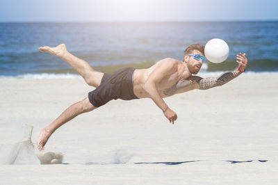 Full length of shirtless man jumping on beach