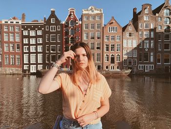 Portrait of beautiful woman standing by building against canal