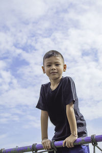 Portrait of boy standing by railing against sky