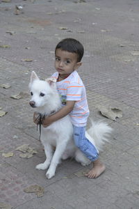 Portrait of cute baby boy sitting on a dog on the footpath and holding the dog with his neck