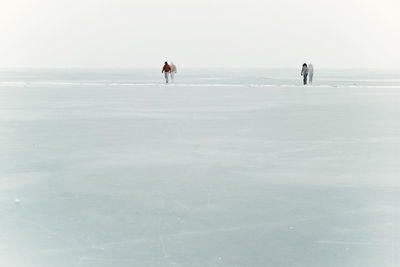 People walking on snow covered beach against clear sky