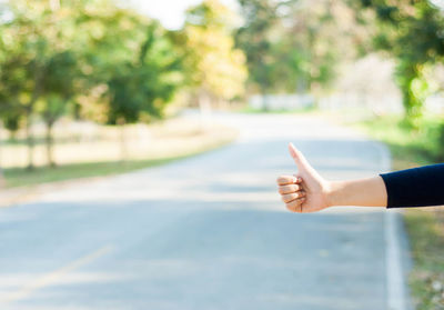 Cropped image of woman hand hitchhiking at roadside
