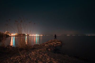 Man standing on rocks in lake against sky at night