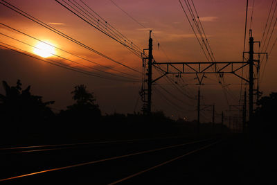 Silhouette electricity pylons against sky during sunset