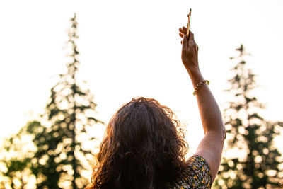 Rear view of woman holding plant against sky