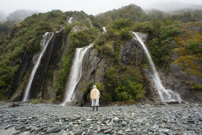 Man standing in front of water fall during misty morning in franz josef glacier hiking trail.