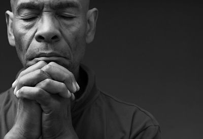 Black man praying to god with hands together on grey background with people stock image stock photo