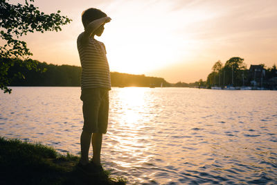 Silhouette woman standing by lake against sky during sunset