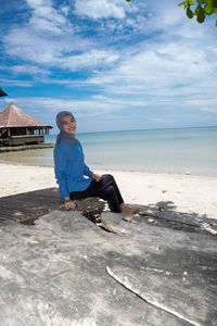 Side view of woman sitting on beach against sky